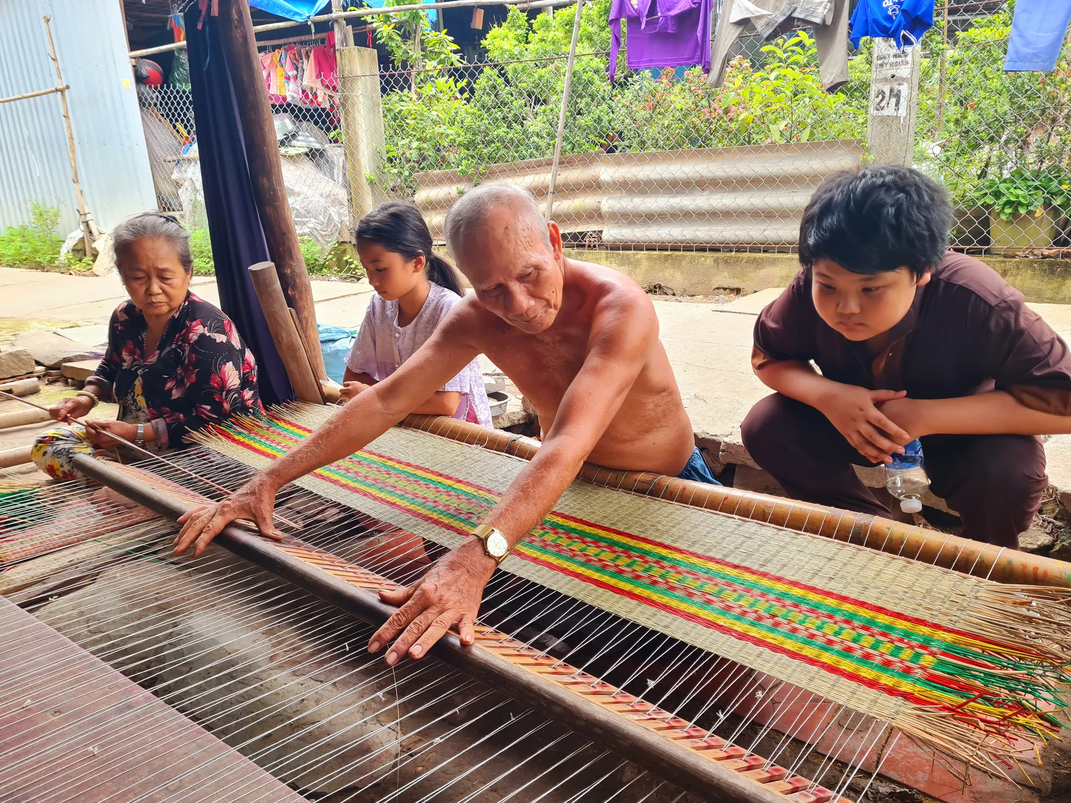 Local artisans and a visitor working around a colourful mat-weaving loom
